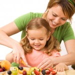 Woman and little girl preparing fruit salad Adults can act as role models to encourage children to eat healthy and stay active.